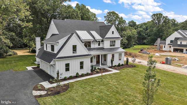 modern farmhouse style home with a standing seam roof, aphalt driveway, board and batten siding, covered porch, and metal roof