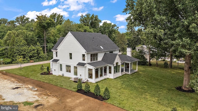 back of house with a lawn, roof with shingles, a chimney, and a sunroom