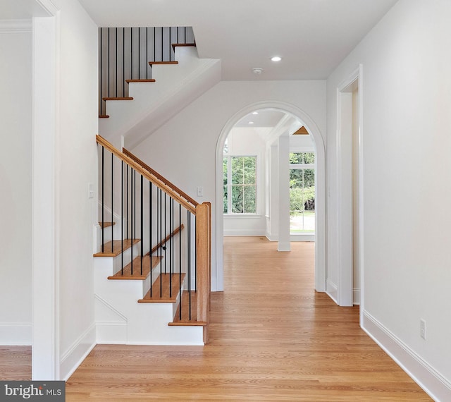 foyer featuring light wood finished floors, recessed lighting, arched walkways, and baseboards