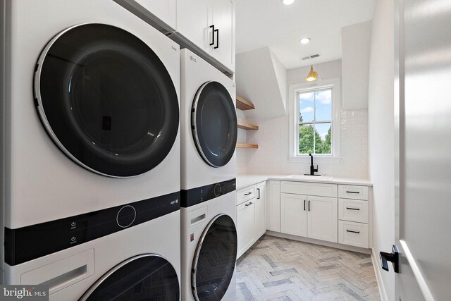 laundry area featuring visible vents, stacked washer and dryer, a sink, recessed lighting, and cabinet space