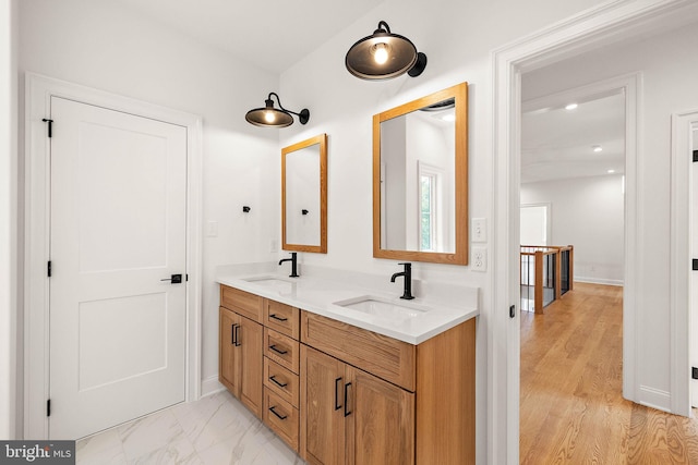 bathroom featuring double vanity, marble finish floor, baseboards, and a sink