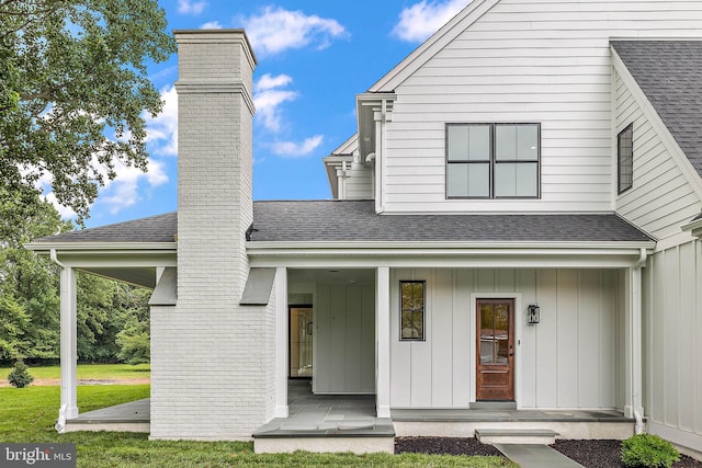 view of front of property featuring a front yard, roof with shingles, a porch, a chimney, and board and batten siding