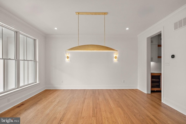 empty room featuring visible vents, crown molding, baseboards, and wood finished floors