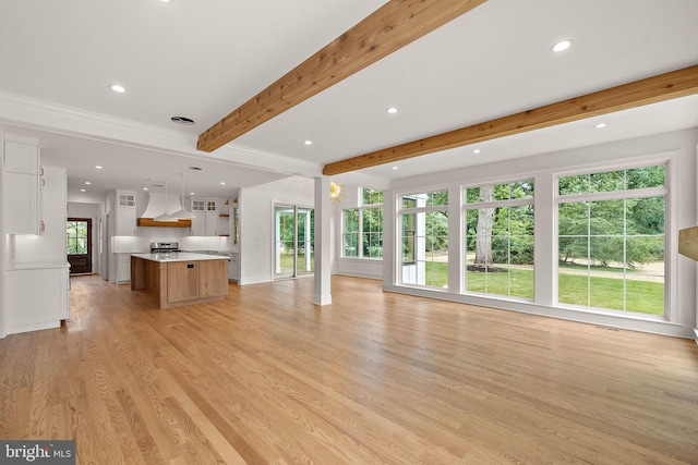 unfurnished living room with beam ceiling, light wood-style flooring, plenty of natural light, and recessed lighting