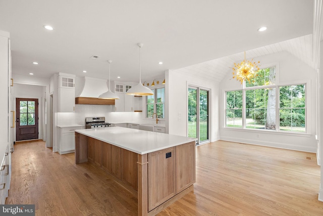 kitchen featuring light countertops, lofted ceiling, light wood-style floors, custom exhaust hood, and stainless steel gas range