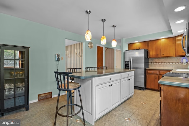 kitchen with tasteful backsplash, baseboards, appliances with stainless steel finishes, white cabinetry, and a kitchen breakfast bar