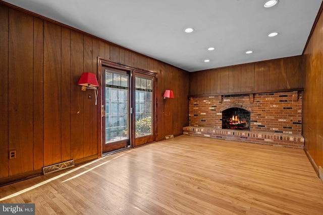 unfurnished living room with light wood-style flooring, wood walls, a brick fireplace, and visible vents