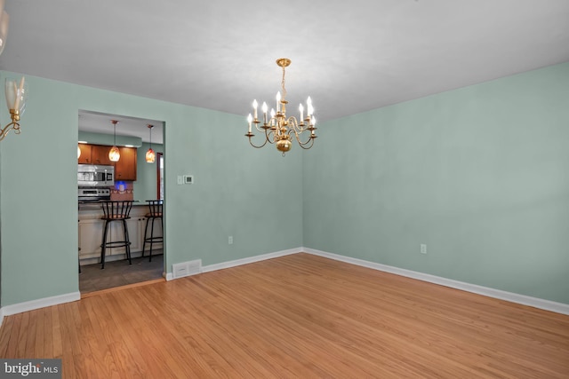 unfurnished dining area featuring baseboards, visible vents, light wood finished floors, and an inviting chandelier