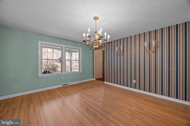 unfurnished room featuring a chandelier, visible vents, baseboards, and wood finished floors