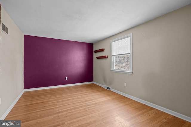 empty room featuring light wood finished floors, baseboards, and visible vents