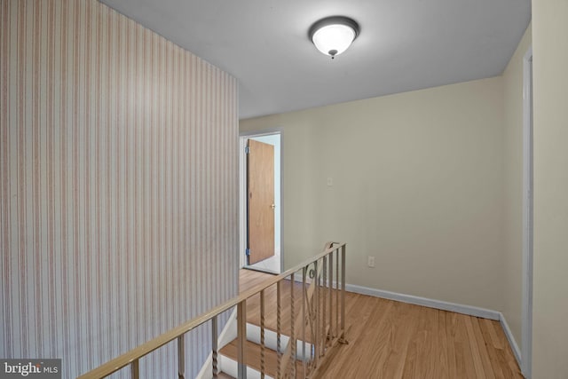 hall with baseboards, light wood finished floors, and an upstairs landing