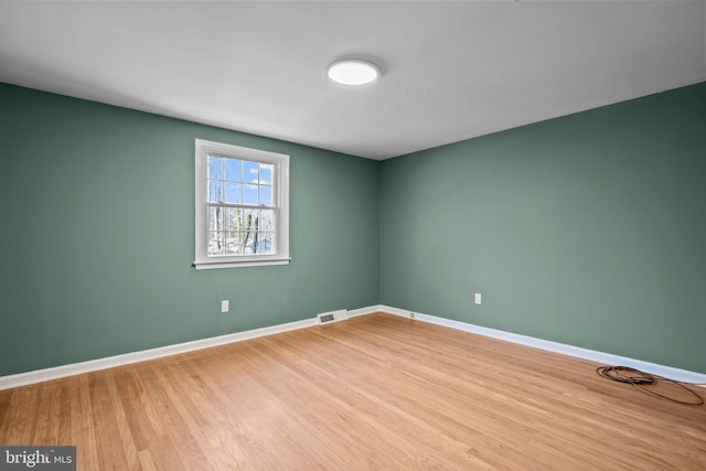 spare room with baseboards, visible vents, and wood finished floors