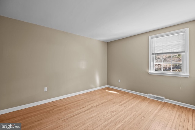 spare room with wood finished floors, visible vents, and baseboards