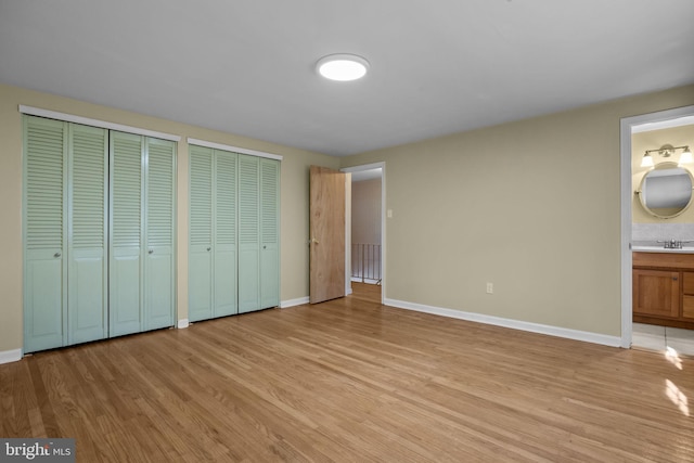 unfurnished bedroom featuring multiple closets, light wood-style floors, ensuite bath, and baseboards