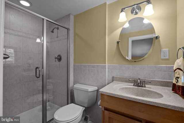 bathroom with toilet, vanity, tile walls, wainscoting, and a shower stall