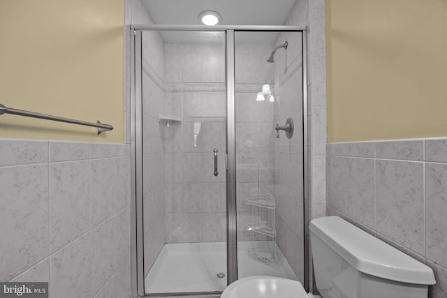 bathroom featuring a stall shower, wainscoting, tile walls, and toilet