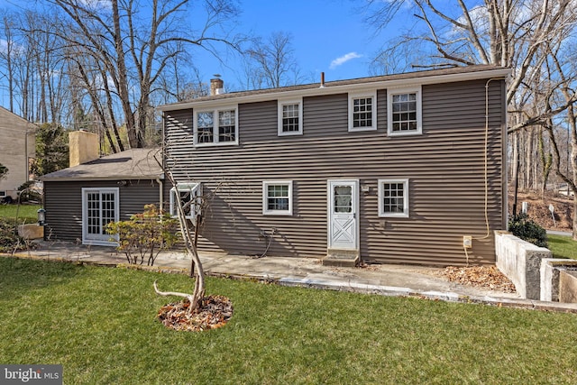 back of property featuring a chimney, a patio area, and a lawn