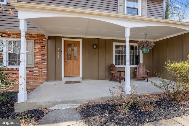 doorway to property featuring covered porch, brick siding, and board and batten siding