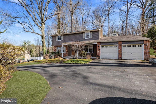 colonial-style house featuring aphalt driveway, brick siding, fence, and an attached garage