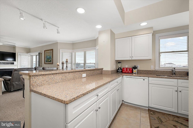 kitchen featuring light stone counters, white dishwasher, a peninsula, a sink, and white cabinets