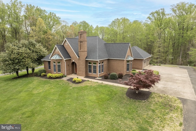 view of front facade with driveway, a chimney, roof with shingles, a front yard, and brick siding