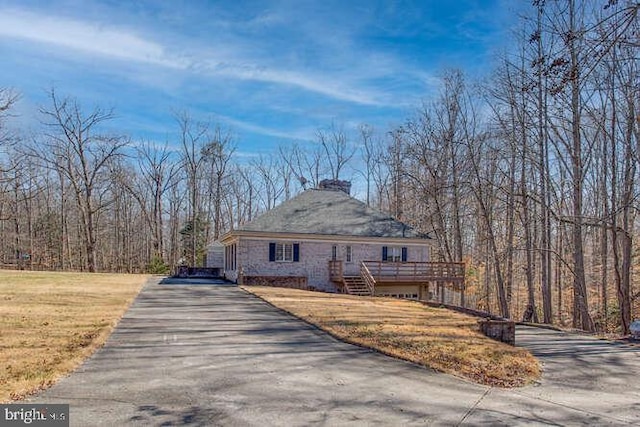 view of property exterior with driveway, a lawn, and a wooden deck