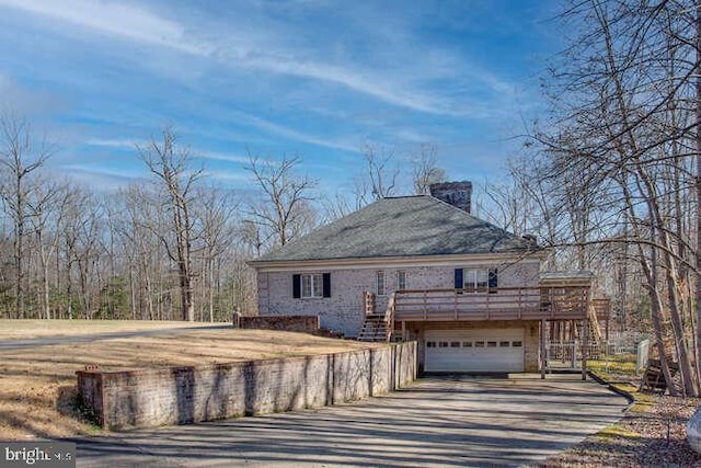 view of side of property with a deck, driveway, a chimney, and a garage