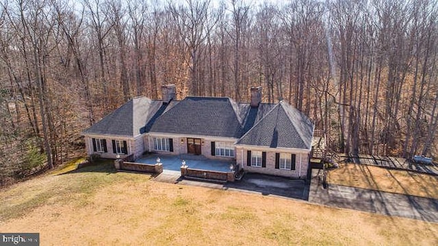 exterior space with a chimney, a lawn, a view of trees, and a patio