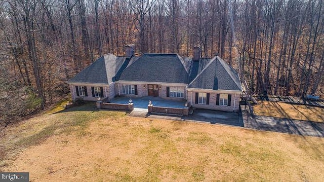 view of front of house featuring a patio area, a chimney, a front lawn, and a view of trees