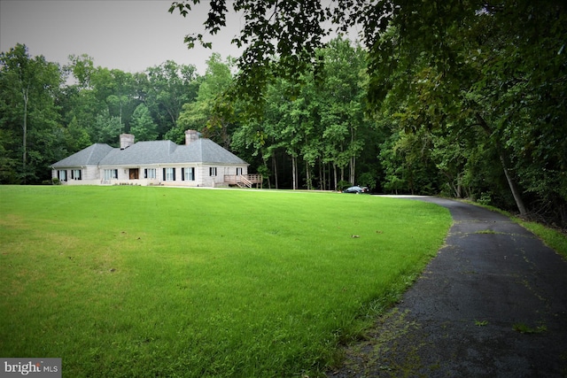 view of front facade featuring a front yard, a chimney, and a forest view