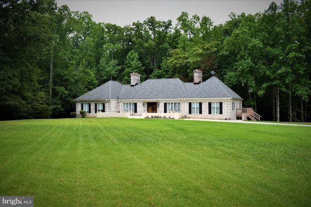 ranch-style home with a front lawn, a chimney, and a wooded view