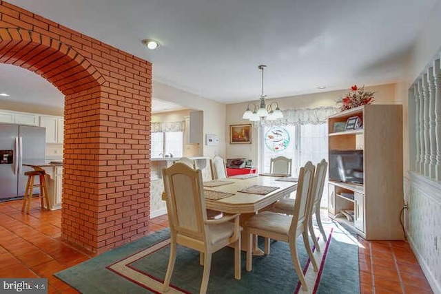 dining space with brick wall, arched walkways, a notable chandelier, and light tile patterned flooring