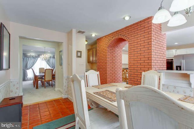 dining space featuring visible vents, brick wall, tile patterned flooring, carpet floors, and a chandelier