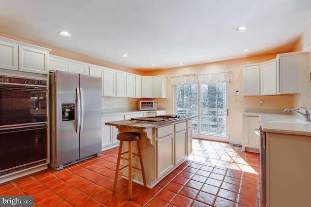 kitchen featuring dobule oven black, stainless steel fridge, tile patterned flooring, and a sink