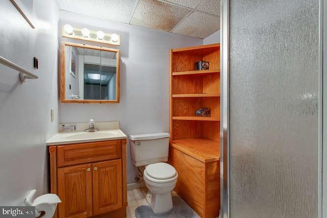 bathroom with a drop ceiling, vanity, toilet, and an enclosed shower