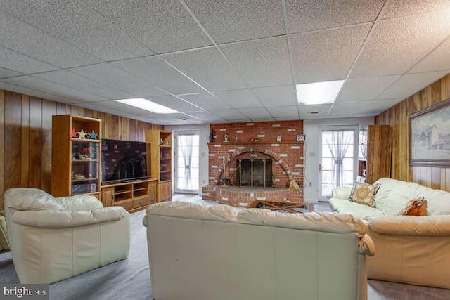 carpeted living area featuring a drop ceiling, wood walls, and a fireplace