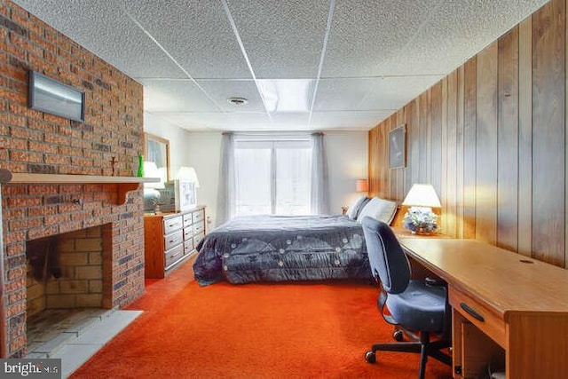 bedroom featuring carpet floors, a paneled ceiling, a brick fireplace, and wooden walls