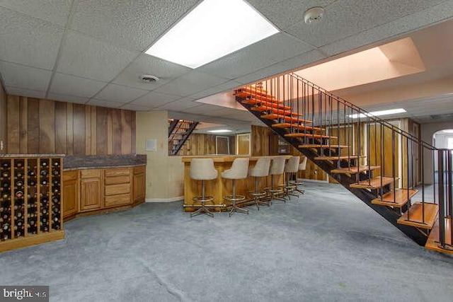 bar with visible vents, wooden walls, a bar, a drop ceiling, and stairs