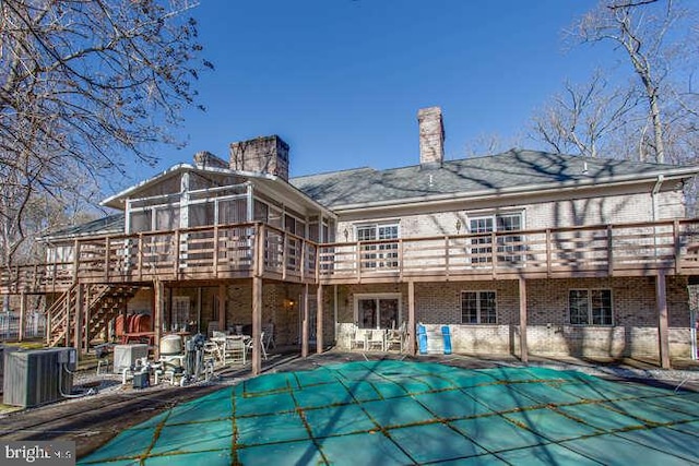 back of property with a patio, brick siding, a wooden deck, and a covered pool