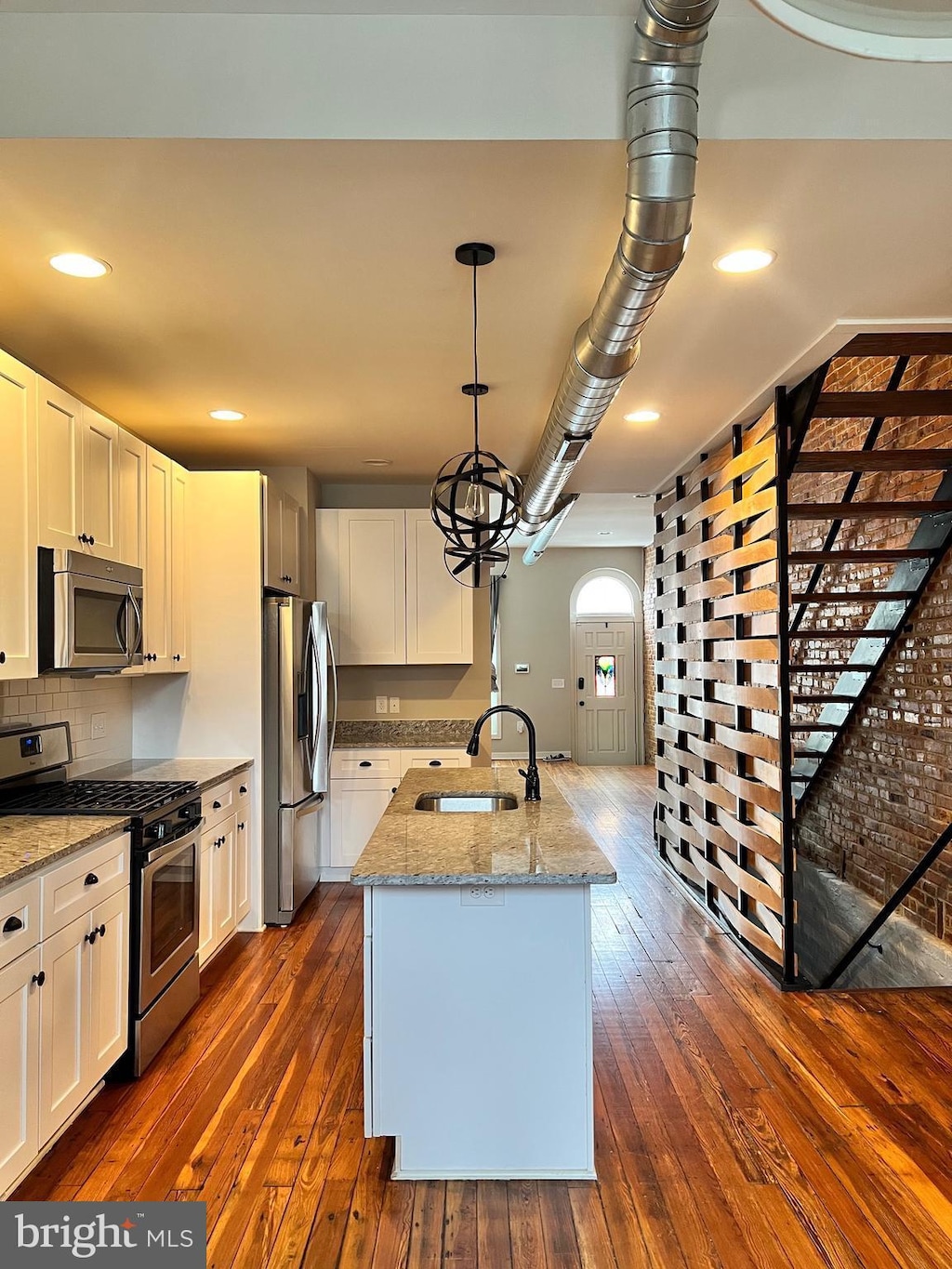 kitchen featuring stainless steel appliances, dark wood-style flooring, a sink, and light stone counters