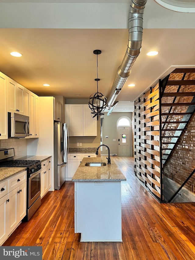 kitchen featuring stainless steel appliances, dark wood-style flooring, a sink, and light stone counters