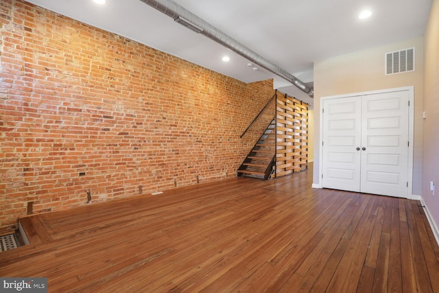 basement featuring hardwood / wood-style floors, stairway, baseboards, visible vents, and brick wall