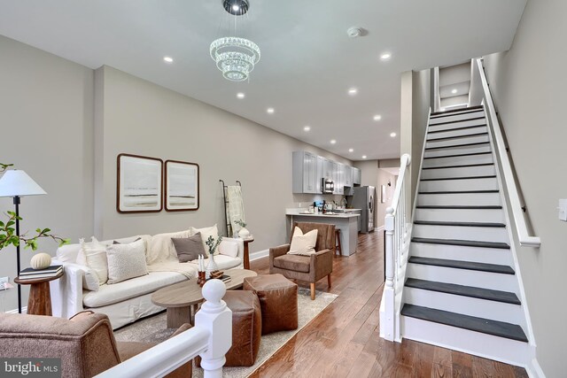 living area with recessed lighting, stairway, an inviting chandelier, baseboards, and hardwood / wood-style flooring