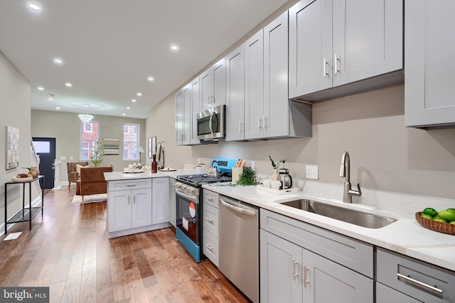 kitchen with light wood finished floors, stainless steel appliances, light countertops, a sink, and a peninsula