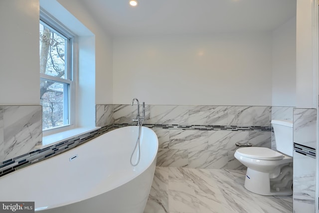 full bathroom featuring toilet, a wainscoted wall, marble finish floor, a freestanding tub, and recessed lighting