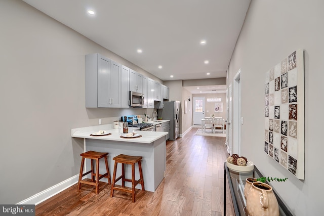 kitchen featuring stainless steel appliances, light countertops, light wood-style floors, a sink, and a kitchen bar