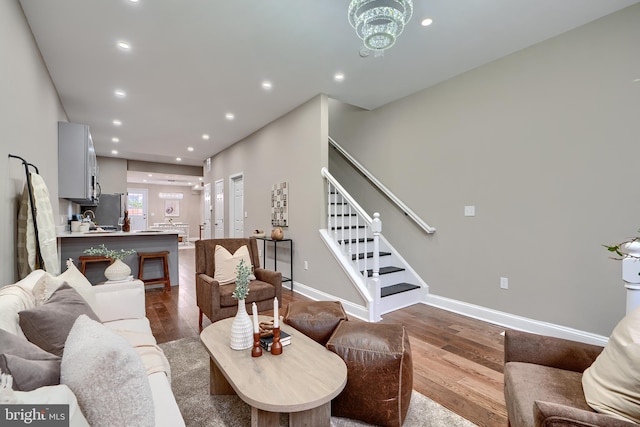 living area featuring recessed lighting, dark wood-type flooring, baseboards, stairs, and an inviting chandelier