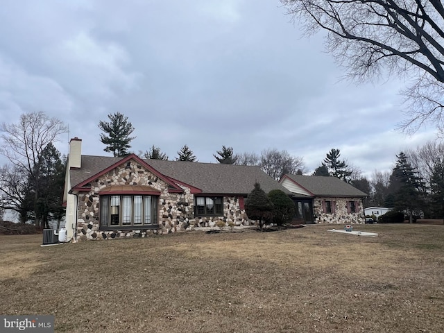 view of front of property featuring a front yard, stone siding, central AC, and a chimney