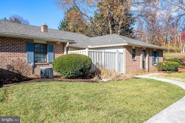 view of home's exterior featuring cooling unit, a garage, brick siding, a yard, and a chimney