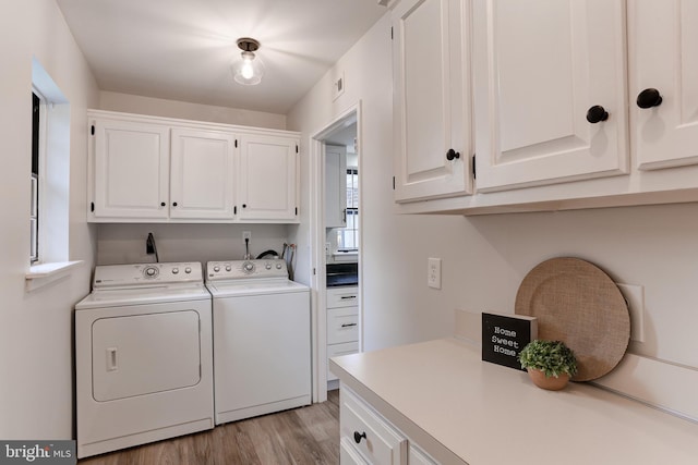 clothes washing area featuring light wood finished floors, washer and clothes dryer, and cabinet space